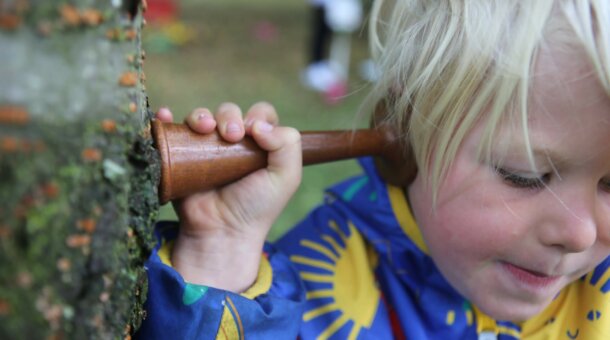 child listening to a tree with a wooden ear cone